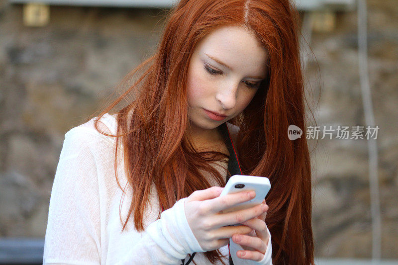 照片中，一个14 / 15岁的红发少女，皮肤苍白，脸上有雀斑，坐在教堂里专注地盯着手机屏幕，穿着上蜡的夹克